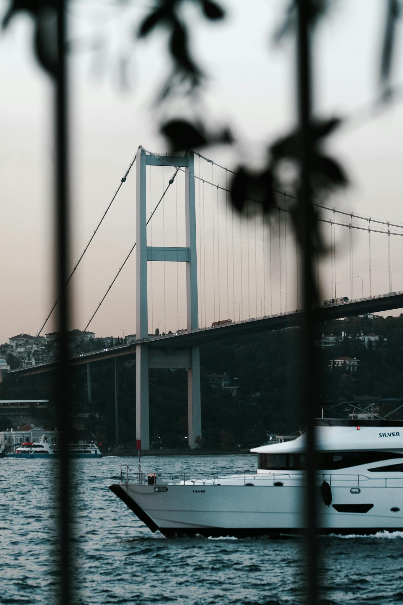 View of the iconic Bosphorus Bridge with a yacht passing by at twilight in Istanbul.
